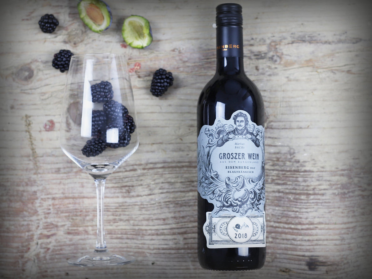 Das Bild zeigt eine Flasche Groszer Wein Eisenberg DAC Blaufränkisch, neben einem Weinglas mit Brombeeren und einer aufgeschnittenen Pflaume. Die stilvolle Präsentation unterstreicht die Qualität des Weins und eignet sich perfekt für Weinliebhaber, Gourmet-Abende oder als Geschenk