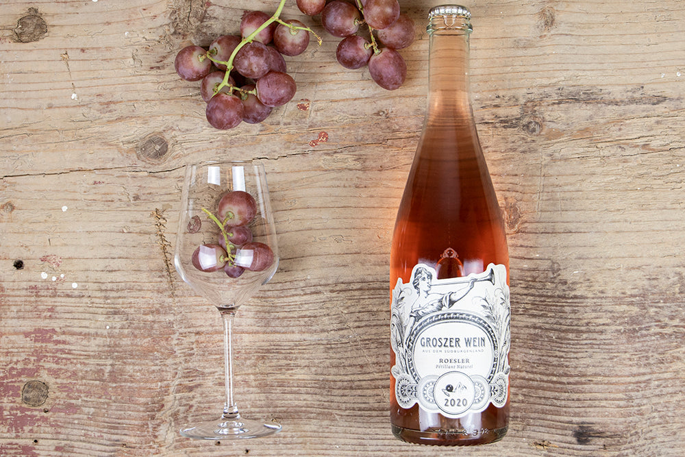 Das Bild zeigt Pet Nat Rösler Perlwein Rosé, Jahrgang 2020, aus dem Südburgenland in Österreich vom Weingut Groszer Wein. Der natürliche Perlwein überzeugt mit feinperliger Eleganz, fruchtigen Noten und eignet sich perfekt als Aperitif, zu festlichen Anlässen oder als Geschenk für Weinliebhaber.
