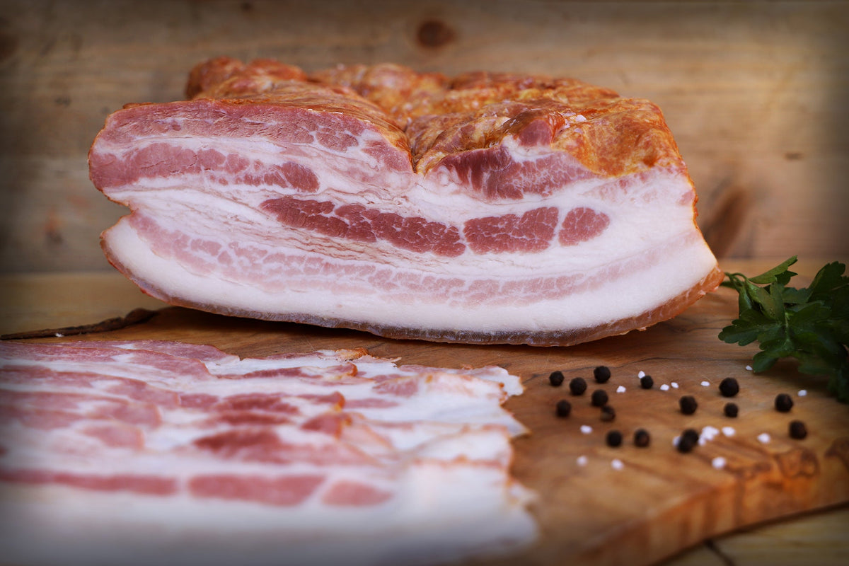 Das Bild zeigt unseren Land.Luft Bio Frühstücksspeck am Stück, bereits geschnitten und auf einem Holzbrett angerichtet. Die hochwertige Speck-Spezialität eignet sich perfekt für Frühstück, Brotzeit, Brunch oder herzhafte Rezepte.