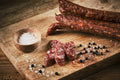 Auf dem Bild sind mehrere Land.Luft Pfefferbeißer Bio Salamis zu sehen, die auf einem Holzbrett angerichtet sind. 
Ideal für Brotzeit, Wurstplatten oder als herzhafter Snack