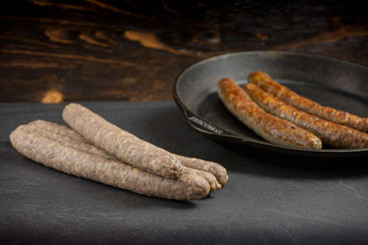 Auf dem Bild ist Land.Luft Bio Rinderbratwurst zu sehen. Einmal frisch und einmal gebraten angerichtet, saftig und aromatisch. Ideal zum Grillen und zum Braten.
