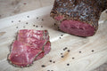 Das Bild zeigt aufgeschnittenen Rinder-Pfefferschinken, ummantelt mit geschrotetem Bio-Pfeffer (ca. 180–220 g). Die hochwertige Spezialität eignet sich perfekt für Brotzeit, Wurstplatten oder als delikater Snack für Feinschmecker